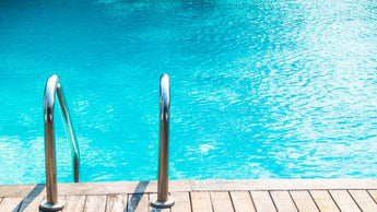 Nahaufnahme eines Swimmingpools mit klarem blauen Wasser, Metallgeländern und einem Holzdeck in hellem Sonnenlicht.