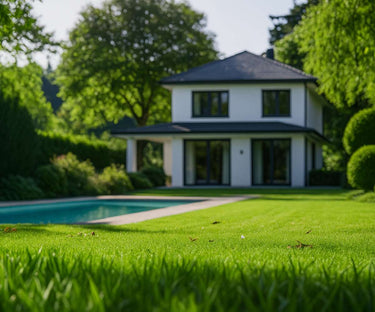 Im Hintergrund steht ein modernes zweistöckiges Haus mit großen Fenstern, umgeben von üppig grünen Bäumen. Im Vordergrund befinden sich ein gepflegter Rasen und ein rechteckiger Swimmingpool. Die Szene sieht heiter und sonnig aus.