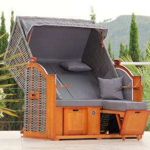Der klassische 2-Sitzer von DERKORB: Wetterfester Strandkorb mit grauen Kissen, Holzrahmen, Arm- und Fußstützen sowie Seitentischen – für maritimes Urlaubsgefühl auf Ihrer Terrasse.