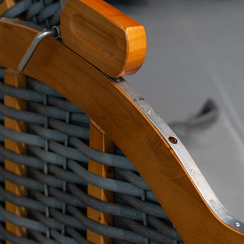 Nahaufnahme eines Stuhls mit Holz- und Metallgestell und blaugrauen geflochtenen Riemen, die die detailreiche Handwerkskunst und die glatte Holzoberfläche zeigen.