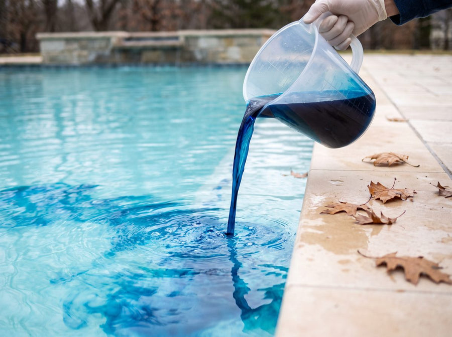 Blaues Pool Wintermittel wird aus einem Messbecher ins Beckenwasser gegeben