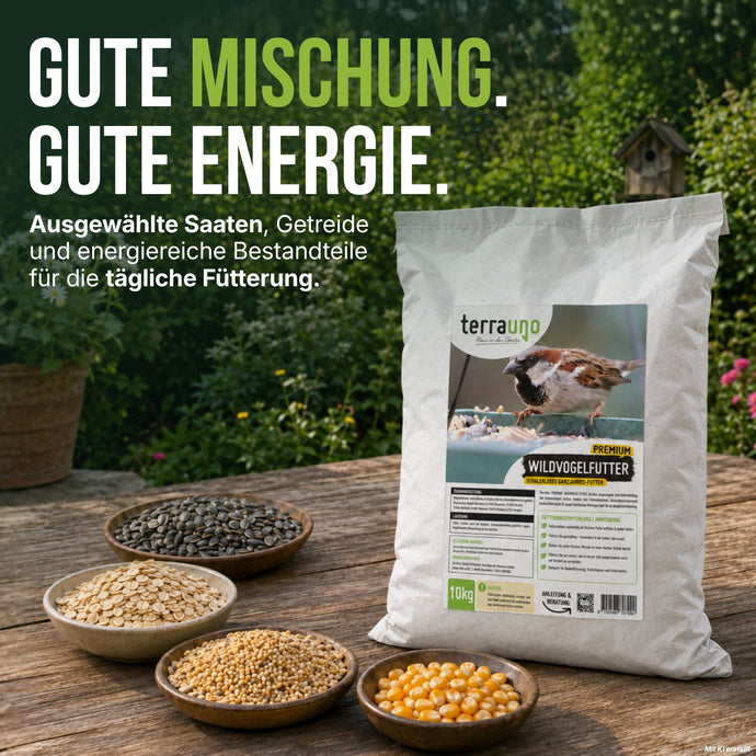 Auf einem Tisch im Freien steht eine Tüte „TerraUno Premium Wildvogelfutter“, umgeben von Schalen, die mit Samen und Körnern gefüllt sind. Auf der Verpackung ist ein Vogel abgebildet, und ein deutscher Text beschreibt dieses nahrhafte, schalenlose Vogelfutter als ideales Ganzjahresfutter für Wildvögel. Im Hintergrund bildet üppiges Grün eine natürliche Kulisse.